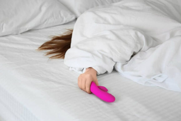 Girl under sheets using rabbit style vibrator sex toys