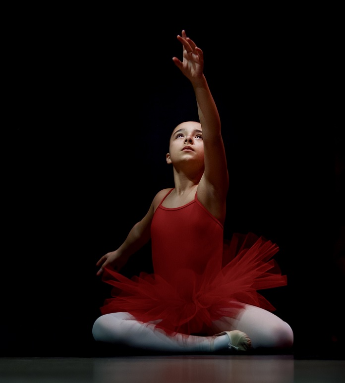 picture of a girl sitting on the floor, dancing ballet, wearing a red leotard and a tutu