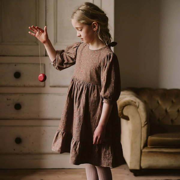 little girl wearing brown cotton dress and playing with red yoyo