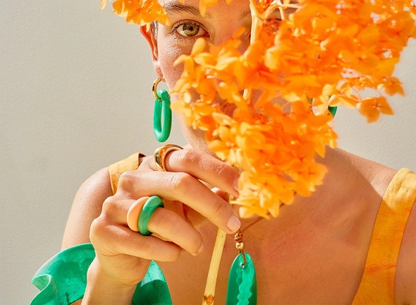 picture of woman wearing resin jewellery designer pieces holding an orange flower 