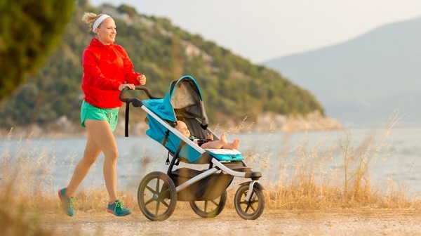 woman jogging in nature with a baby in a running pram