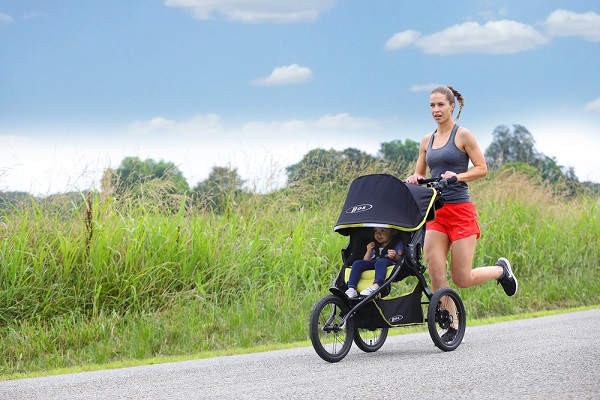 woman jogging in nature with baby in running stroller 