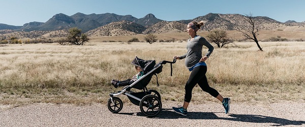 woman jogging in nature with baby in a jogging stroller 